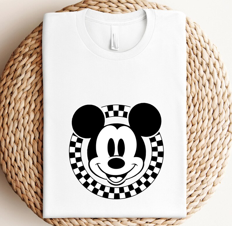 May include: A white t-shirt with a black and white checkered circle design featuring Mickey Mouse's face in the center.