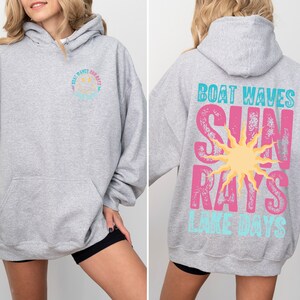 May include: Grey hooded sweatshirt with a graphic design on the back that says "Boat Waves Sun Rays Lake Days" in pink, blue, and yellow. The front of the sweatshirt has a smaller graphic design of a smiley face with the text "Boat Waves Sun Rays" in blue and pink.