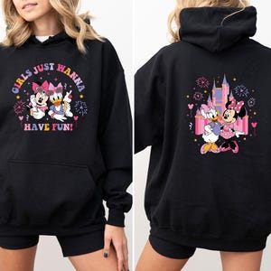 K&ouml;nnte beinhalten: Schwarzer Kapuzenpullover mit Minnie Mouse und Daisy Duck. Auf der Vorderseite steht "Girls Just Wanna Have Fun!" mit den Figuren. Auf der R&uuml;ckseite sind die Figuren vor einem Schloss mit Feuerwerk zu sehen.