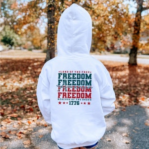 May include: White hooded sweatshirt with a red, white and blue graphic print that says "Land of the Free, Freedom, Freedom, America, Freedom, Because of the Brave, 1776".