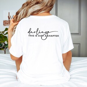 May include: White t-shirt with black text that reads "darling, this is just a chapter" with a small heart symbol.