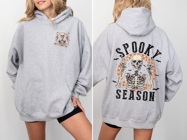 May include: A light gray hoodie with a front pocket and hood. The front features a small graphic of a skeleton. The back displays a larger design with a skeleton, bats, and the words "Spooky Season."