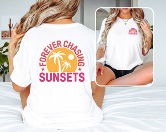 May include: White t-shirt with a pink and yellow graphic on the back that says "Forever Chasing Sunsets" with palm trees and a sun. The graphic is in a circle.
