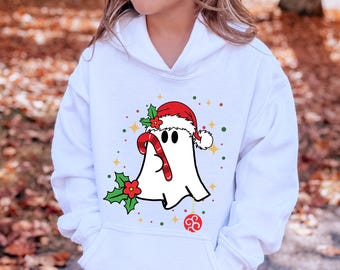 May include: White hooded sweatshirt featuring a cartoon ghost wearing a Santa hat and holding a candy cane. The ghost is decorated with holly and a red ornament. The design includes colorful stars and dots, perfect for the holiday season.
