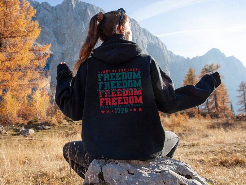 May include: Black hooded sweatshirt with a red, white and blue graphic print that says "Land of the Free, Freedom, Freedom, America, Freedom, Freedom, Because of the Brave, 1776".