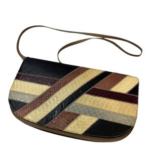 May include: A rectangular shoulder bag with a patchwork design. The bag features a variety of colors and textures, including black, brown, beige, and gray. The bag has a brown strap and a zipper closure.