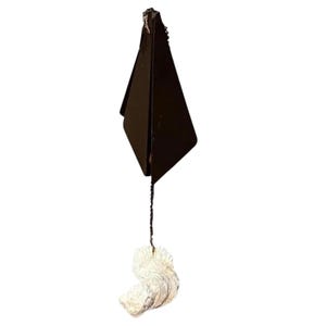 May include: A dark brown wind chime with a geometric shape and a textured, off-white seashell. The wind chime is suspended by a thin, dark string.