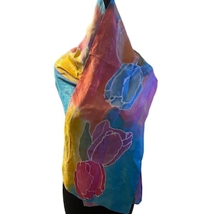 May include: A colorful silk scarf with a floral tulip design. The scarf features a vibrant mix of colors, including yellow, blue, pink, and purple. The tulip design is outlined in white, adding contrast to the scarf's overall appearance.