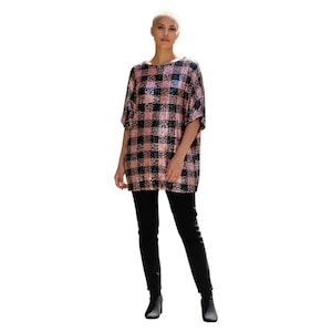 May include: A short-sleeved, oversized top with a pink and black plaid pattern. The top is paired with black pants and black ankle boots. The outfit is a casual, yet stylish ensemble.