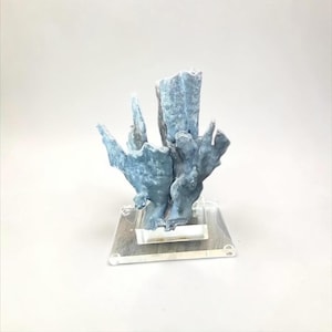 May include: A blue-grey, coral-like sculpture on a clear acrylic base. The sculpture has a textured surface with multiple spiky protrusions. The artwork is displayed against a white background, highlighting its unique form and color.