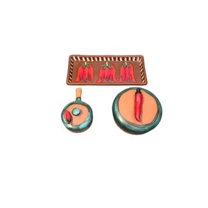 May include: A set of three ceramic pieces: a rectangular tray and two round dishes. The tray and dishes are brown with red chili pepper designs. The dishes have teal and orange accents. The tray measures approximately 10 inches long.