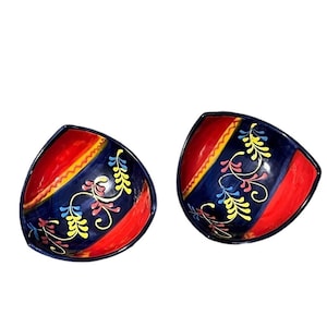 May include: Two decorative ceramic bowls. Each bowl has a red interior and a blue exterior with a yellow stripe and floral design. The bowls are triangular in shape and have a glossy finish.