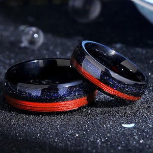 May include: Two black and red rings with a blue and silver glitter finish. The rings are made of tungsten carbide and have a red inlay.