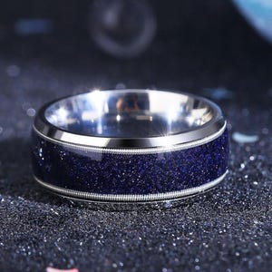 Könnte beinhalten: Ein silberner Ring mit einem dunkelblauen Band. Das Band besteht aus einem glitzernden Material, das einem Sternenhimmel ähnelt.