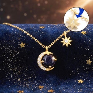 May include: A gold-coloured necklace with a crescent moon pendant holding a dark blue stone, and a star pendant with a clear gem. The necklace includes a small star charm with the letter "A". The chain is delicate, set against a dark blue background with gold stars.