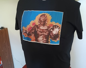May include: Black t-shirt with a graphic print of a creature from the black lagoon surrounded by sunflowers. The creature is green and has a menacing expression.