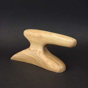 May include: A wooden sculpture with a unique, abstract design. The sculpture is made of light brown wood with a natural grain pattern. It has a smooth, rounded surface and a curved shape.