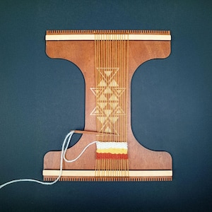 May include: A wooden weaving loom with a geometric design. The loom is brown with a light-colored stripe at the top and bottom. The weaving has a small section of woven threads in white, yellow, and red. A white thread is attached to the weaving.