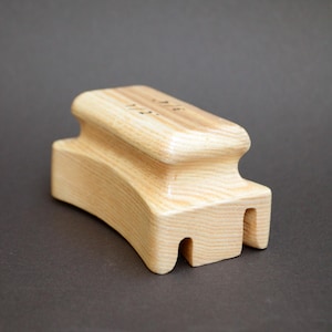 May include: A wooden tool with a curved top and two prongs on the bottom. The tool is made of light wood with a natural grain.