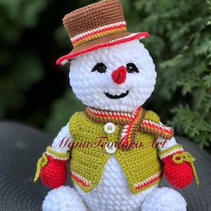 May include: A white crocheted snowman wearing a brown and green hat, a green vest with red and white stripes, and red mittens. The snowman has a red nose and black eyes.