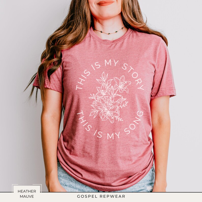 May include: Heather mauve t-shirt with the text "THIS IS MY STORY, THIS IS MY SONG" in a circular design around a floral illustration. The shirt is a short-sleeved crew neck.