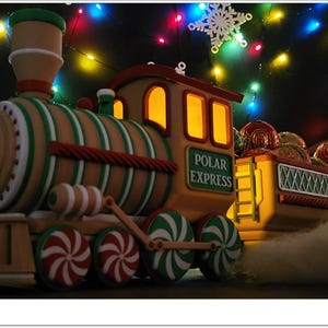 May include: A gingerbread-themed toy train with candy cane wheels and a light-up engine. The train is decorated with green and red stripes and says "Polar Express" on the side. The train is surrounded by Christmas lights.