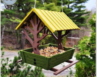 May include: A bird feeder with a yellow roof and brown tree branches. The feeder is filled with birdseed and has a green base. The feeder is hanging from a string.