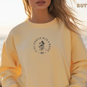 May include: A yellow sweatshirt featuring a black and white graphic of Mickey Mouse. The graphic is a circle with the text "It all started with a mouse" and the year "1928".