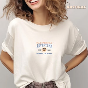 May include: White t-shirt with a blue and orange graphic that says "California Adventure Est. 2001 Anaheim, California" with a Mickey Mouse head inside a sun.