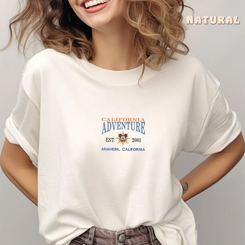 May include: White t-shirt with a blue and orange graphic that says "California Adventure Est. 2001 Anaheim, California" with a Mickey Mouse head inside a sun.