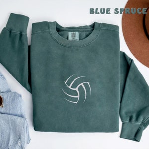 May include: A dark green sweatshirt with a white volleyball graphic. The sweatshirt is laid flat on a white surface.
