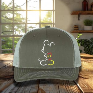 May include: A green and gray trucker hat with a white outline of Mickey Mouse's head and red and yellow accents. The hat has a mesh back.