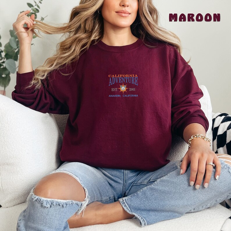 May include: A maroon sweatshirt with a graphic design that says "California Adventure Est. 2001 Anaheim, California".
