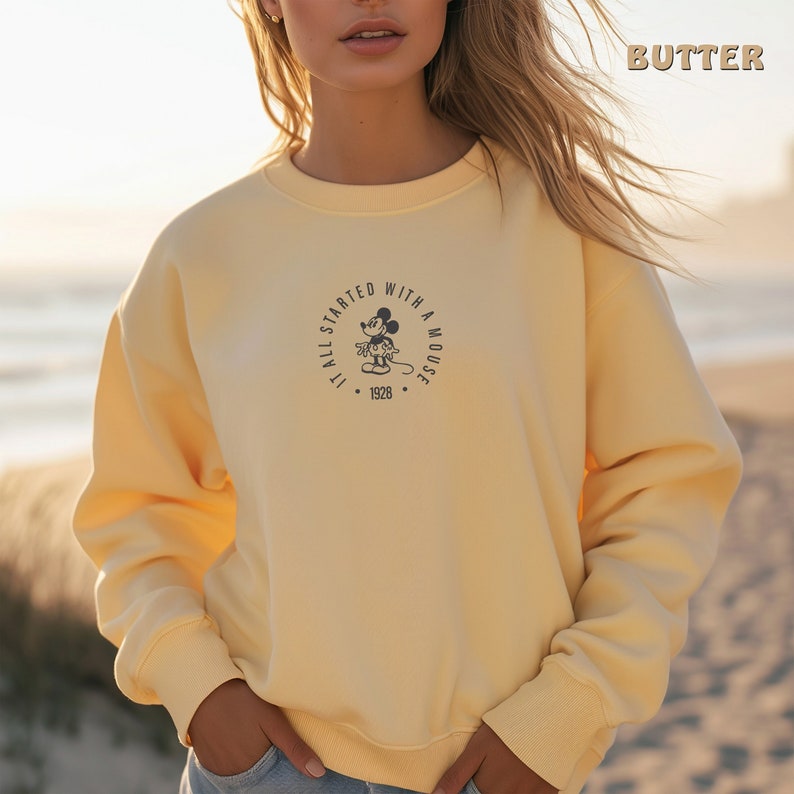 May include: A yellow sweatshirt featuring a black and white graphic of Mickey Mouse. The graphic is a circle with the text "It all started with a mouse" and the year "1928".