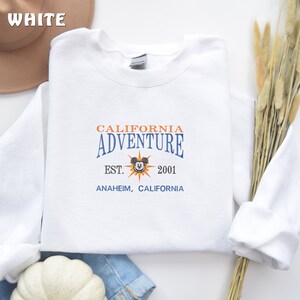 May include: White sweatshirt with a blue and orange graphic that says "California Adventure" with Mickey Mouse's head in the middle. The graphic also says "Est. 2001" and "Anaheim, California."