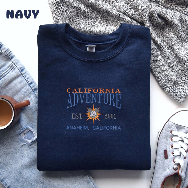 May include: A navy blue sweatshirt with the text "CALIFORNIA ADVENTURE EST. 2001 ANAHEIM, CALIFORNIA" and a Mickey Mouse head graphic.