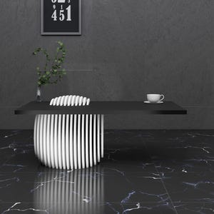 May include: A black and white modern desk with a white cup and saucer on the surface. The desk is in a room with a black marble floor and a gray wall. There is a plant in a vase on the left side of the image.