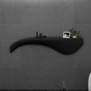 May include: A black, wavy, wall-mounted shelf with a picture frame, small decorative objects, and a small potted plant on top.