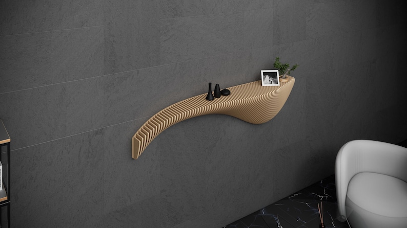 May include: A curved wooden shelf with a slatted design, mounted on a gray wall. The shelf has a small plant, a picture frame, and three black decorative objects on it.