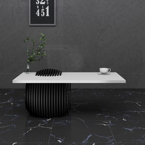 May include: A white table with a black, geometric base sits on a black and white marble floor. A white cup sits on the table.