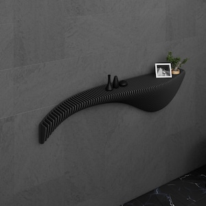 May include: A black, curved wall shelf with a slatted design. The shelf has a small plant, two black decorative items, and a framed photo on it.