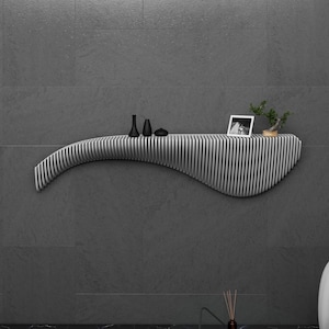 May include: A white, curved, wall-mounted shelf with black and white vertical stripes. The shelf has a small black and white photo, two black vases, and a small potted plant on top.