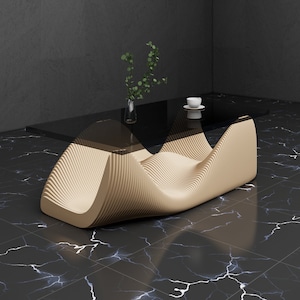 Op de afbeelding: Een moderne salontafel met een golvend, organisch ontwerp. De tafel heeft een glazen blad en een beige houten basis. De tafel staat op een zwart-witte marmeren vloer.