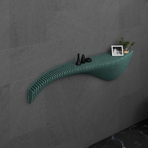 May include: A teal green, curved, wall-mounted shelf with a wood-like texture. The shelf has a small plant and two black decorative items on it.