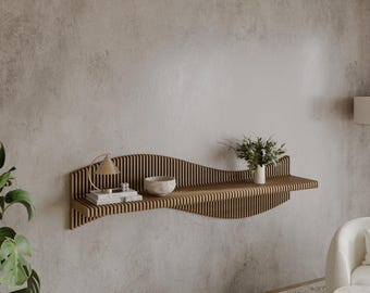 May include: A wooden wall shelf with a wavy design. The shelf has a light brown finish and is mounted on a gray wall. There is a small lamp, a bowl, and a book on the shelf.