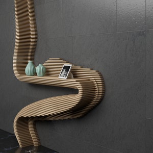 May include: A wooden shelf unit with a unique, curved design. The shelf is made of thin, layered wood and has a light brown finish. It features two small, teal vases and a framed photo.
