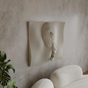 Op de afbeelding: Een beige wandsculptuur met een 3D-ontwerp van een gezicht. De sculptuur is gemaakt van gelaagd hout en heeft een golvende, organische vorm.