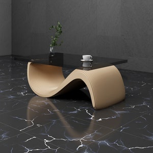 May include: A modern coffee table with a wavy, beige wood base and a black glass top. The table is sitting on a black and white marble floor.