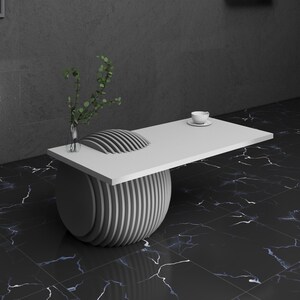 May include: A white coffee table with a round, layered base and a rectangular top. The table is on a black and white marble floor.