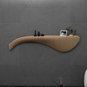 May include: A curved wooden shelf with a wavy design, mounted on a gray wall. The shelf has a small black vase, a black and white photo, and a small potted plant on top.